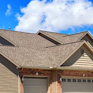 Photo of new asphalt shingles on a two story home. Blue sky and clouds are in the background.